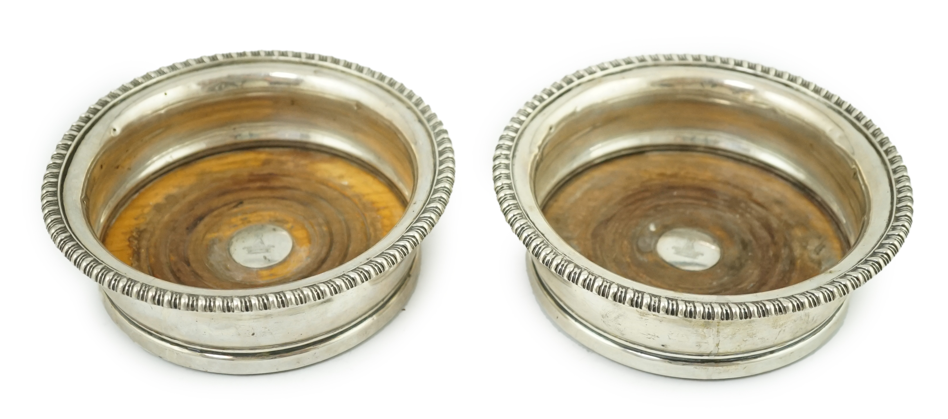 A pair of George III silver wine coasters, by Thomas & John Settle, with gadrooned borders and turned wooden bases, Sheffield, 1821, diameter 15.7cm. Condition - poor to fair